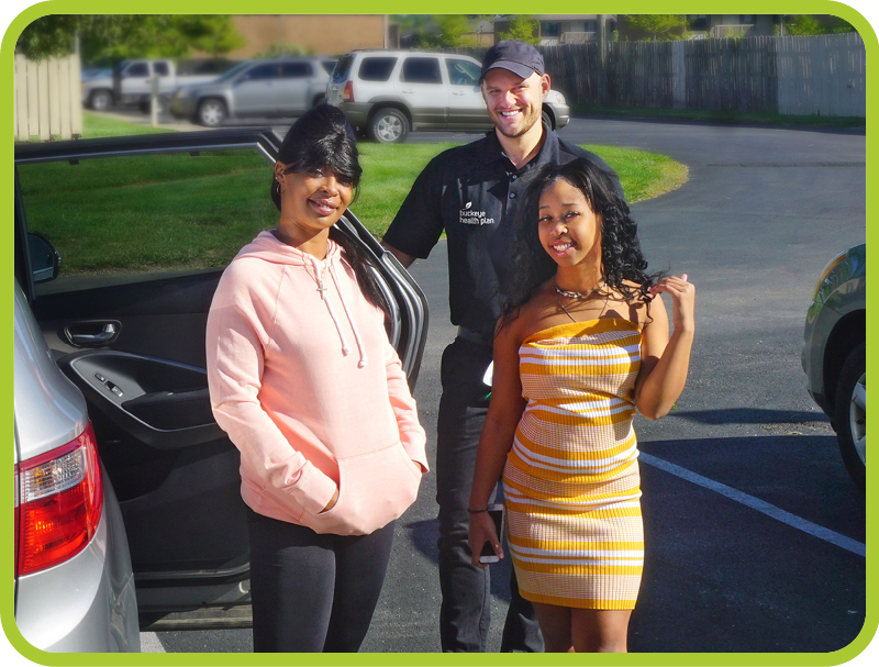 A man poses with two female members outside of their transportation vehicle.