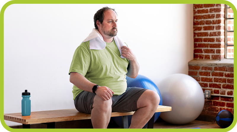 Man sitting in gym with towel and water bottle. 
