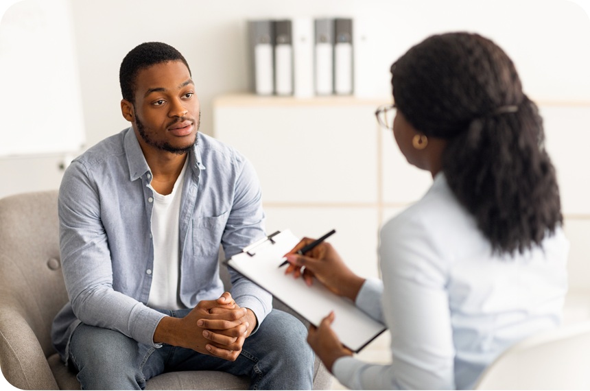 A man talks with a woman who is holding a clipboard and taking notes.