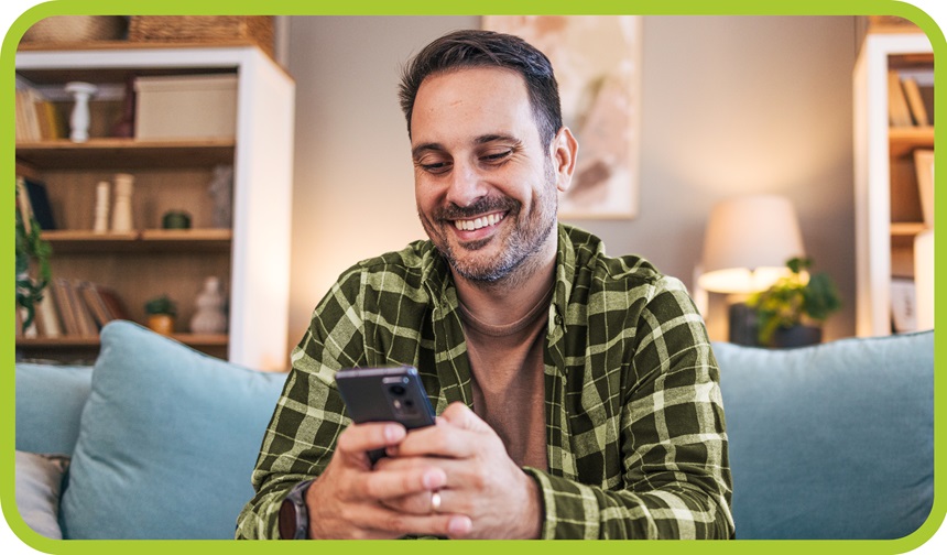 Smiling man looks at phone while sitting on couch.